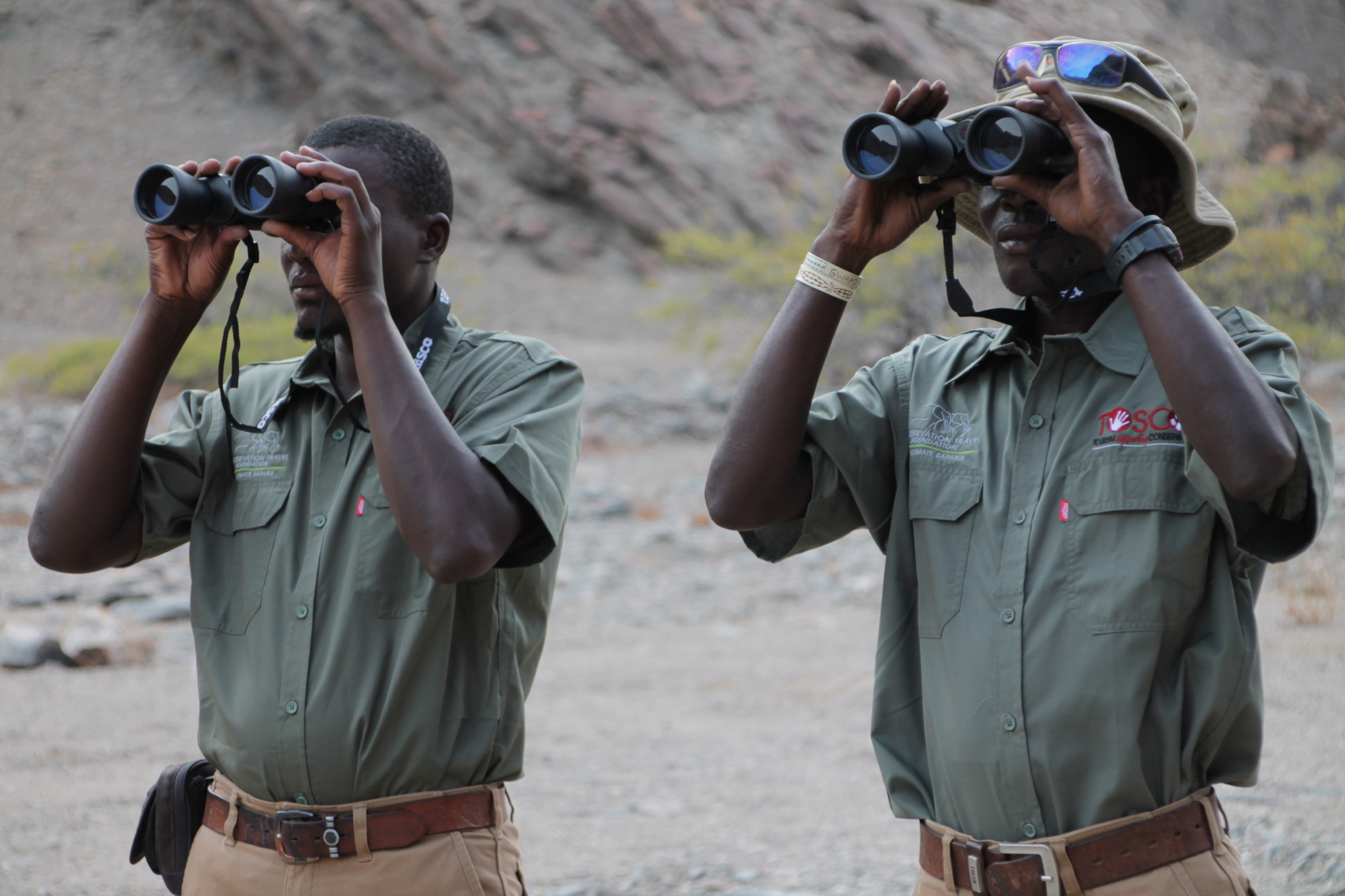 Two lion rangers look intently through their binoculars.
