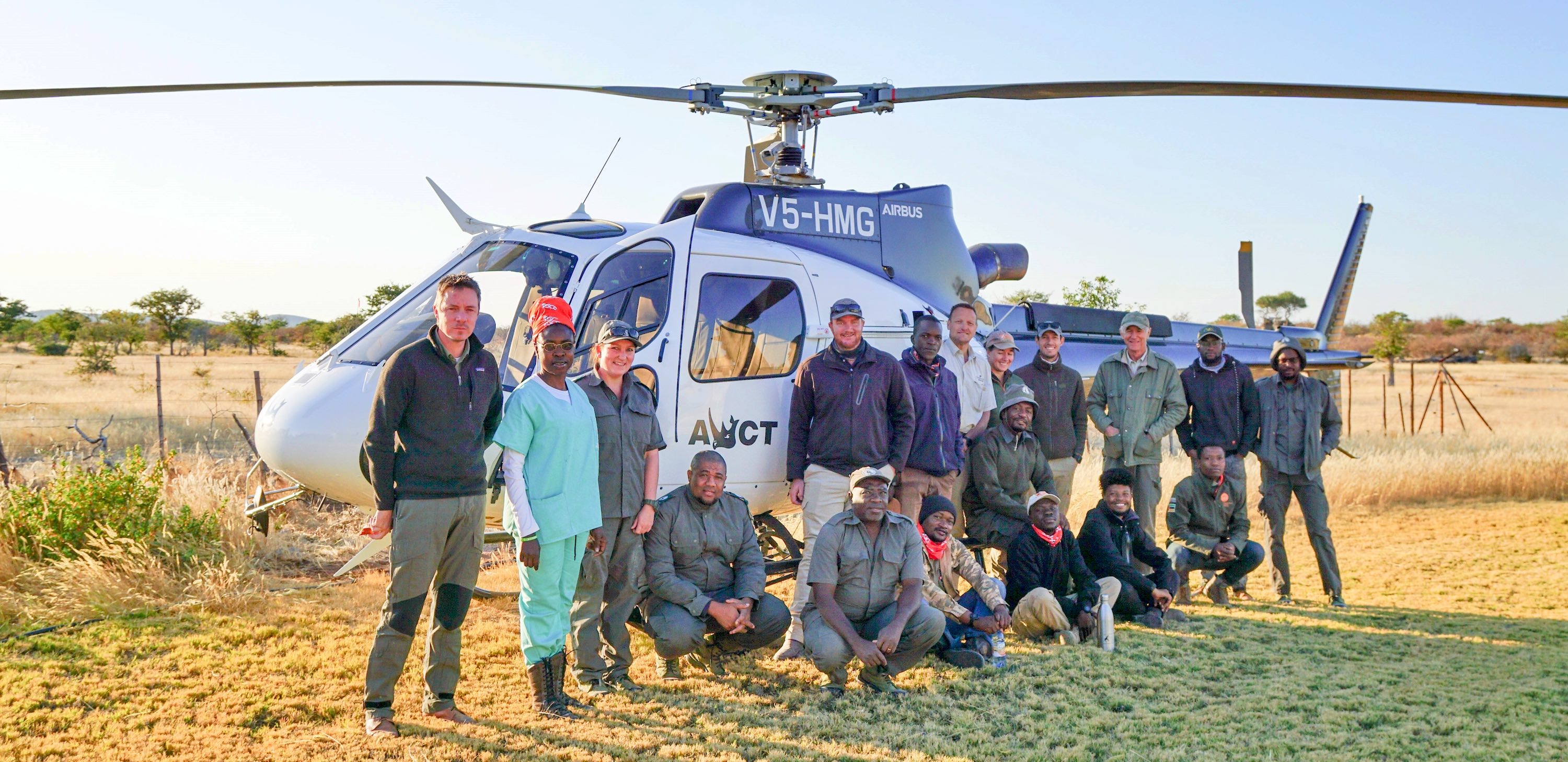 The full group pose in front of the helicopter.